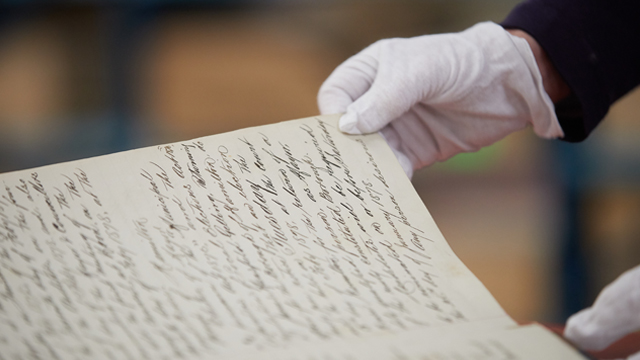 Hands in gloves turning page of old book