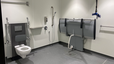 Changing Places bathroom with height adjustable toilet with hand-rails on either side, shower, adult-sized changing table, and hoist.